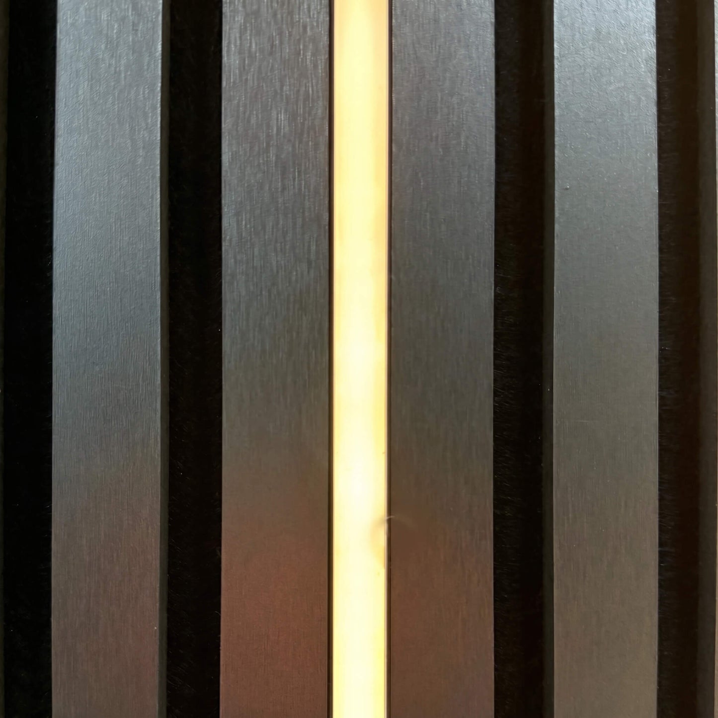 Close-up vertical shot of a 14mm x 11mm dimmable warm white LED lighting strip glowing inside dark charcoal acoustic wood slat paneling with hidden visibility.