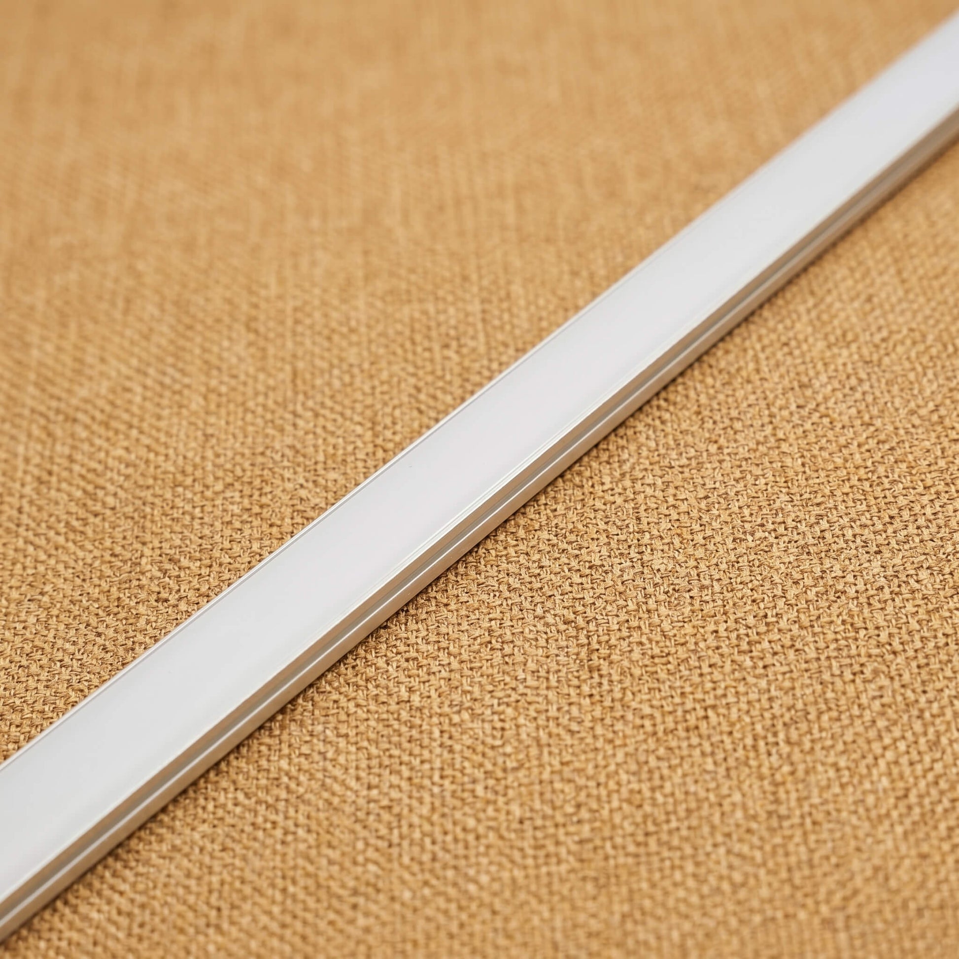 Close-up profile view of a trimless 10mm x 9mm white LED channel strip showcasing the flush-mount installation design on a textured light oak wood background.