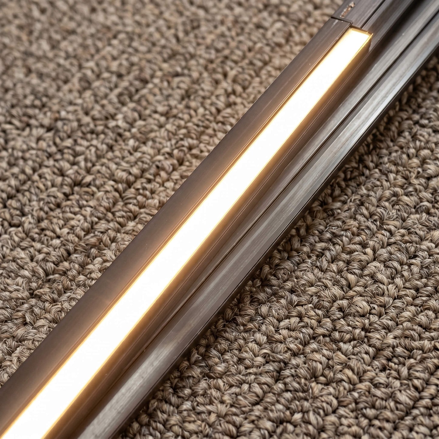 Close-up detail of a 13mm wide slim black LED track channel lit with warm ambient light, showing its seamless, flush profile integrated without a visible edge trim.