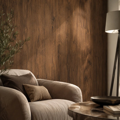 Cozy lounge corner featuring a full-height walnut wood grain PVC wall cladding panel paired with a plush armchair and warm, natural sunlight casting shadows.